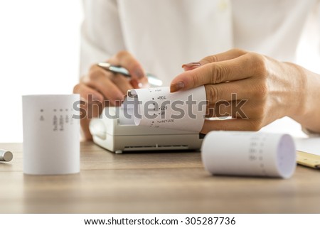 Woman doing calculations on an adding machine or calculator pulling off reams of paper with printed figures and totals, conceptual of accounting a bookkeeping, close up of her hands.