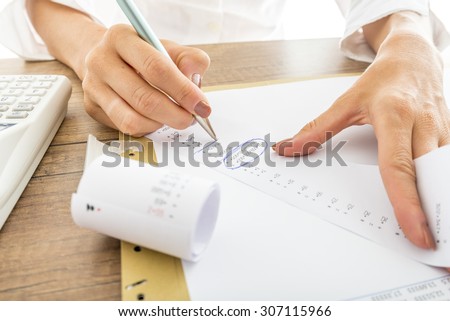 Close up Businesswoman Calculating Expenses on Printed Receipts at her Desk with Calculator on her Side.