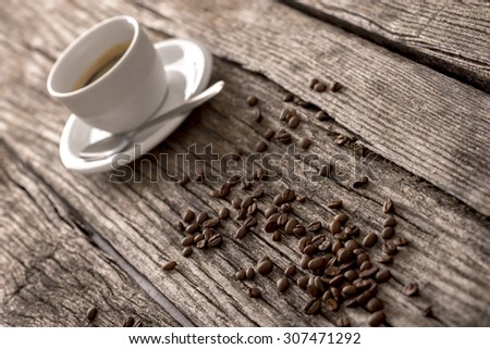 Fresh roasted coffee beans and a cup of black filter coffee or espresso on a rustic wooden table viewed at an angle.
