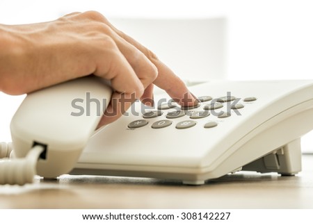 Closeup view of female secretary dialing a telephone number on white landline phone. Conceptual for global communication, technical support and customer service.