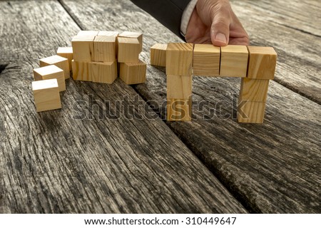 Close up of businessman forming a bridge of small wooden blocks on textured oak desk as he comes to a solution, finding or answer in a conceptual image.