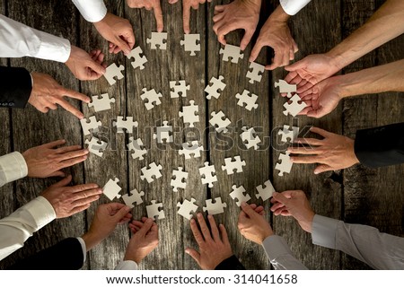 Teamwork Concept - High Angle View of Businessmen Hands Forming Circle and Holding Puzzle Pieces on Top of a Rustic Wooden Table.