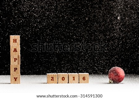 New Year 2016 background with falling snow and a red Christmas bauble with the word Happy spelled out on stacked wooden blocks with the date 2016 alongside over black with copyspace for your greeting.