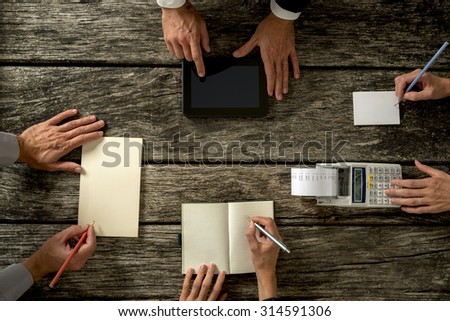 Top View of Businessmen Hands with Holding Notes, Tablet Computer and Printing Calculator on Top of a Rustic Wooden Table.