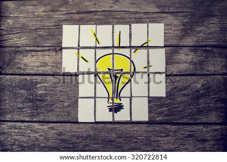 Top view of hand drawn yellow light bulb assembled with many cards over textured rustic boards with a retro faded effect. Conceptual of innovation, research and brainstorming.
