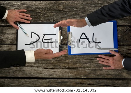 Business deal or transaction concept with the word - Deal - split over two pages of paper on different clipboards with businessmen shaking hands above them, overhead view on a rustic wooden table.