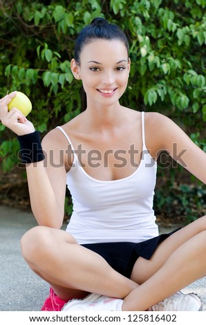 Beautiful brunette girl holding a yellow apple after sports and yoga. Outdoors in the park.