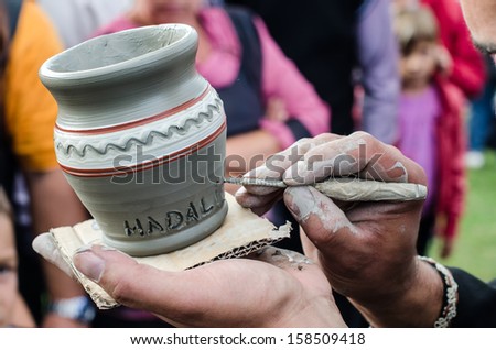Close-up on artist hands personalizing a clay jug by writing the name of a person.