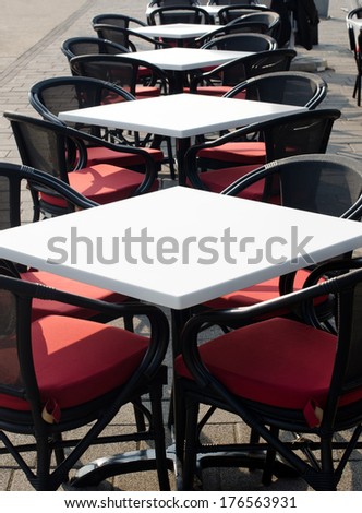 Rows of white empty tables and black wicker chairs in an open air cafeteria. Cafe bar on sunny summer day.