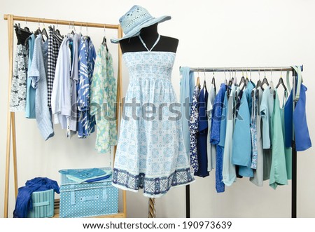 Dressing closet with blue clothes arranged on hangers. A summer dress with hat on a mannequin. Wardrobe full of all shades of blue clothes and accessories.