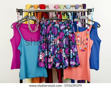 Cute summer outfits displayed on a rack. Wardrobe with colorful summer clothes and accessories. Floral skirt with matching tank tops.