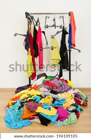 Untidy cluttered woman wardrobe with colorful clothes and accessories. Messy rack of clothes and hangers with a big pile thrown on the ground.