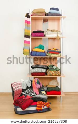 Packing the suitcase for winter vacation. Wardrobe with clothes nicely arranged and a full luggage. Dressing closet with colorful winter clothes and accessories on a shelf.