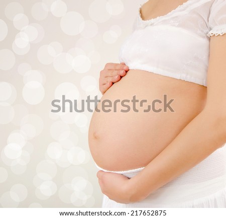 Close up on pregnant belly. Woman expecting a baby dressed in white.