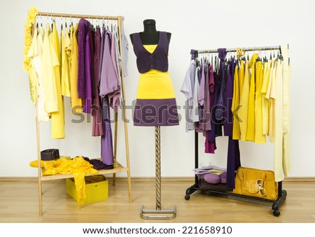 Dressing closet with complementary colors violet and yellow clothes.Wardrobe with purple and yellow clothes arranged on hangers and an outfit on a mannequin.