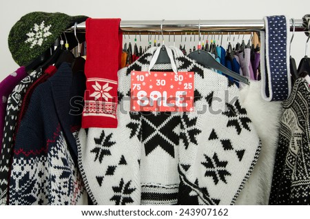 Close up on a big sale sign for winter clothes. Clearance rack with colorful winter outfits and accessories displayed on hangers.