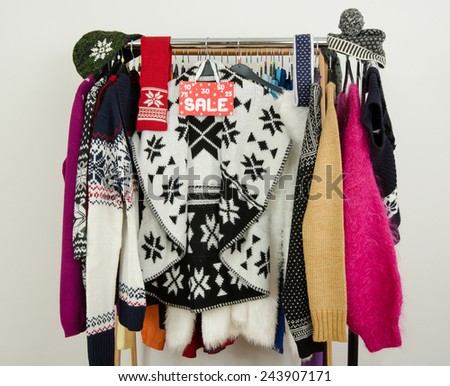 Cute winter sweaters displayed on hangers with a big sale sign. Season clearance rack with colorful winter clothes and accessories.