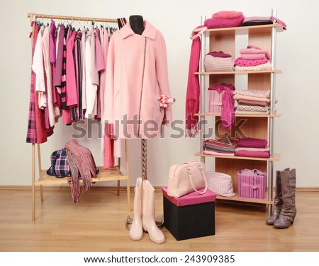 Dressing closet with pink clothes arranged on hangers and shelf, a coat on a mannequin. Fall winter wardrobe full of all shades of pink clothes, shoes and accessories.