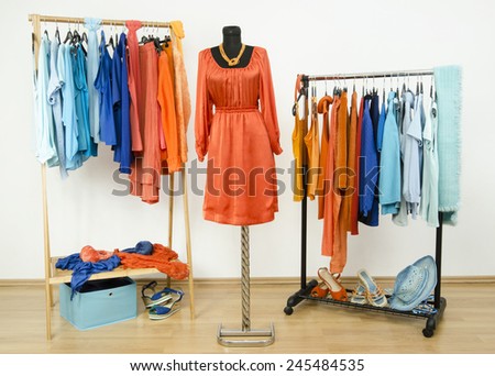Wardrobe with complementary colors orange and blue clothes arranged on hangers. Dressing closet with clothes, shoes and accessories and a dress on a mannequin.