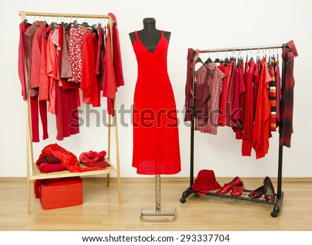 Dressing closet with red clothes arranged on hangers and a dress on a mannequin.  Wardrobe full of all shades of red clothes, shoes and accessories.