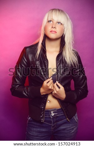 Beautiful blonde in a open leather jacket and jeans  posing on a purple background,  in a studio, fashion photography,