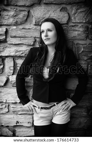 Beautiful brunette in a black blazer, white shirt and shorts posing near the stone wall, in a exterior of building, fashion photography, black and white photo