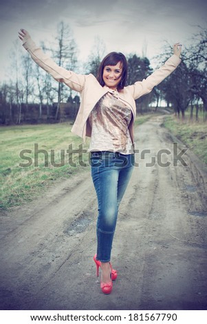 Beautiful brunette in a shirt, jeans and with a blazer posing on a dusty road, in the nature, fashion photography