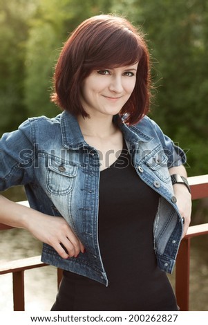 Portrait of beautiful brunette in a denim jacket and black shirt on a bridge, in a nature. Portrait and fashion photography