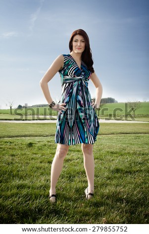 Beautiful brunette is posing on a golf course. She is wearing a dress. Fashion photography.