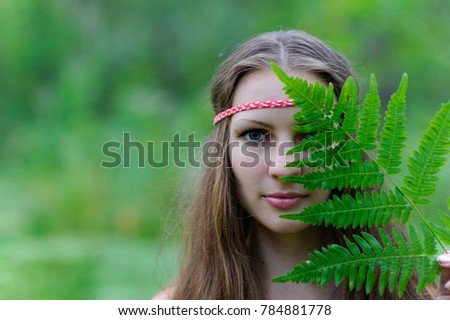 A young beautiful Slavic girl with long hair and Slavic ethnic dress covered her face with a large fern leaf ストックフォト © 