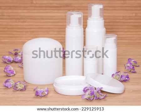 Open jar of cream and other body care cosmetics with flowers  on wooden background
