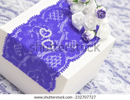 Wedding gift: white gift box decorated with violet lace, white satin roses and small hearts made of beads. Shallow depth of field