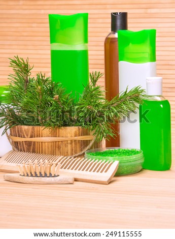 Hair care cosmetics and accessories: basket with pine branches, sea salt, shampoo, conditioner, balm, mask and combs on wooden surface