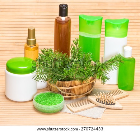 Natural cosmetics and accessories for hair health and beauty: sea salt, shampoo, conditioner, balm, mask, oil, wooden combs with fresh pine branches on wooden surface