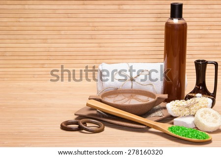 Spa and pampering products and accessories: sea salt, pumice, loofah, wisp of bast, bamboo utensils with water, crock, shower gel, bath towel on wooden surface. Copy space