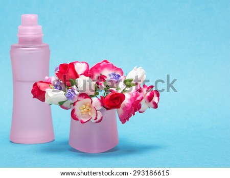 Floral perfume. Close-up of perfume bottle behind bouquet of flowers in its cap. Shallow depth of field, focus on bouquet. Blue background. Copy space