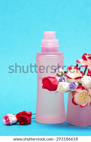 Cropped image of floral perfume. Close-up of perfume bottle behind bouquet of flowers in its cap. Focus on bottle. Blue background