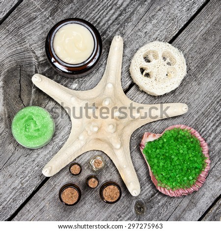 Various spa cosmetics and accessories: sea salt in shell, loofah, skin care cream, natural honey and lemongrass scrub, essential oils with starfish on wooden planks. Top view