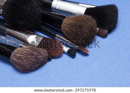 Set of various natural bristle makeup brushes: for applying blush, powder, foundation, cream and compact eyeshadow, kabuki brush. Blue background. Shallow depth of field, focus on first brush bristle