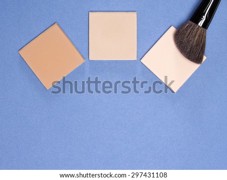 Different shades of compact cosmetic powder with makeup brush on blue background. Copy space