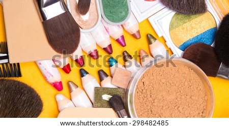 Various makeup cosmetics and accessories: lip liners and eyeliners, loose and compact powder, multicolored eyeshadow, cosmetic sponge and different makeup brushes on bright yellow background