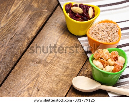 Healthy eating background. Wooden spoon and ceramic cups filled with wheat bran, mixtures of nuts with dried fruits and berries. Peeled hazelnut, almond, papaya, cranberries