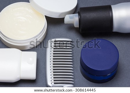 Comb with various hair styling products on gray textured surface