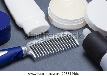 Comb with various hair styling products on gray textured surface. Shallow depth of field