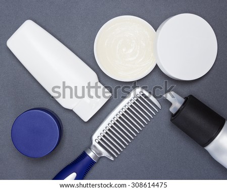 Open jar filled with hair wax and other hair styling products with a comb on gray textured surface