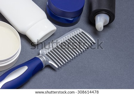 Comb with various hair styling products on gray textured surface. Shallow depth of field. Copy space