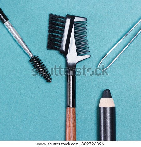 Accessories for care of brows: eyebrow pencil, tweezers, brush and comb on blue background. Eyebrow grooming tools