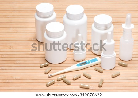 Set of various cold and flu remedies. Jars of medicines, scattered capsules, electronic thermometer, nasal sprays. Small copy space on the left