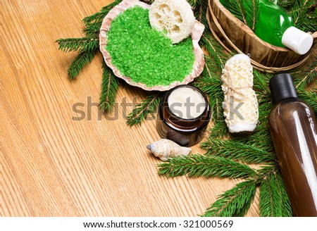 Spa and pampering products and accessories: sea salt in shell, loofah, wisp of bast, skin care cream, shampoo and shower gel in wooden basket surrounded by fir branches. Copy space