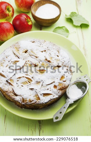 Apple pie with sugar powder and red apples on a wooden table